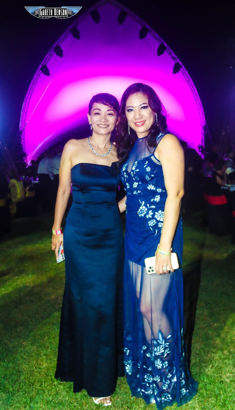 Two women in blue dresses are posing for a picture in front of a purple light.
