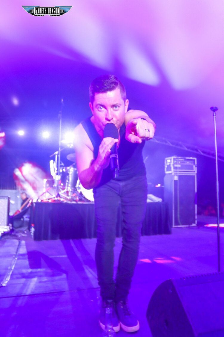 A man singing into a microphone on a stage with purple lights