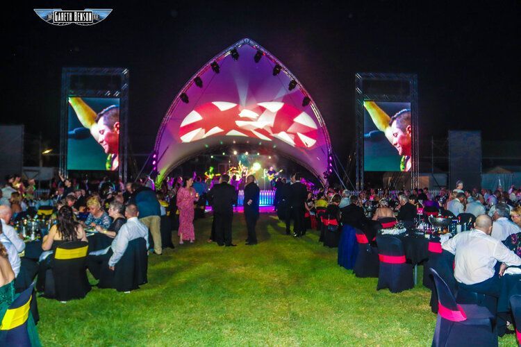 A large group of people are sitting at tables in front of a stage.