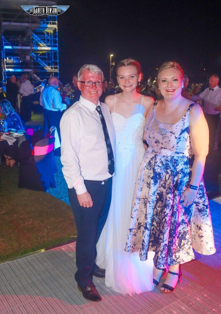A man and two women are posing for a picture at a wedding reception.