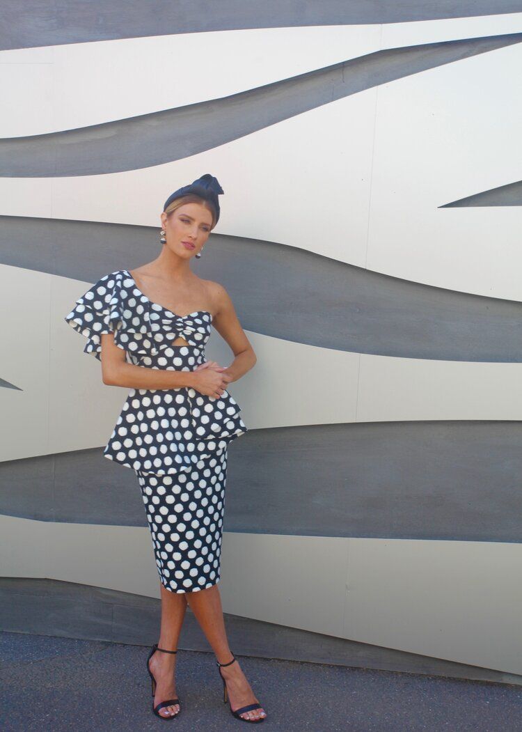 A woman in a black and white polka dot dress is standing in front of a wall