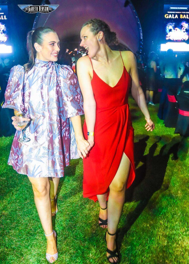 Two women in red dresses are holding hands while standing in the grass.