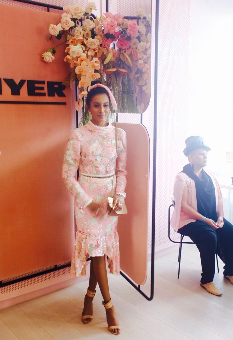 A woman in a pink dress is standing in front of a pink wall.