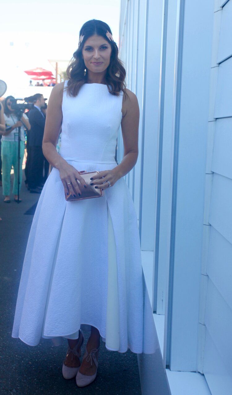 A woman in a white dress is standing in front of a white building.