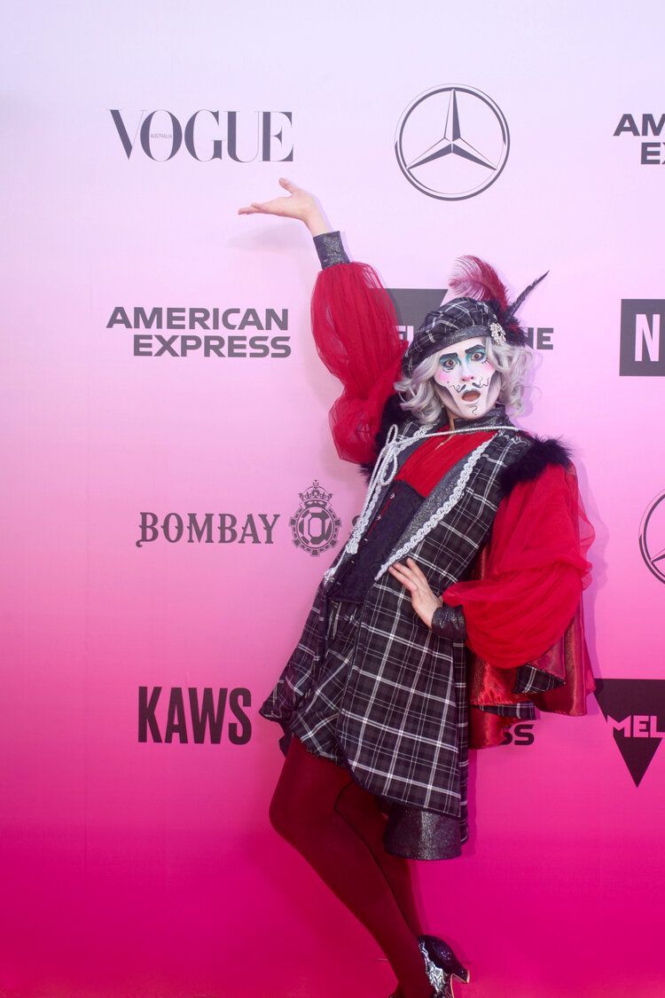 A woman in a clown costume is standing on a pink carpet.