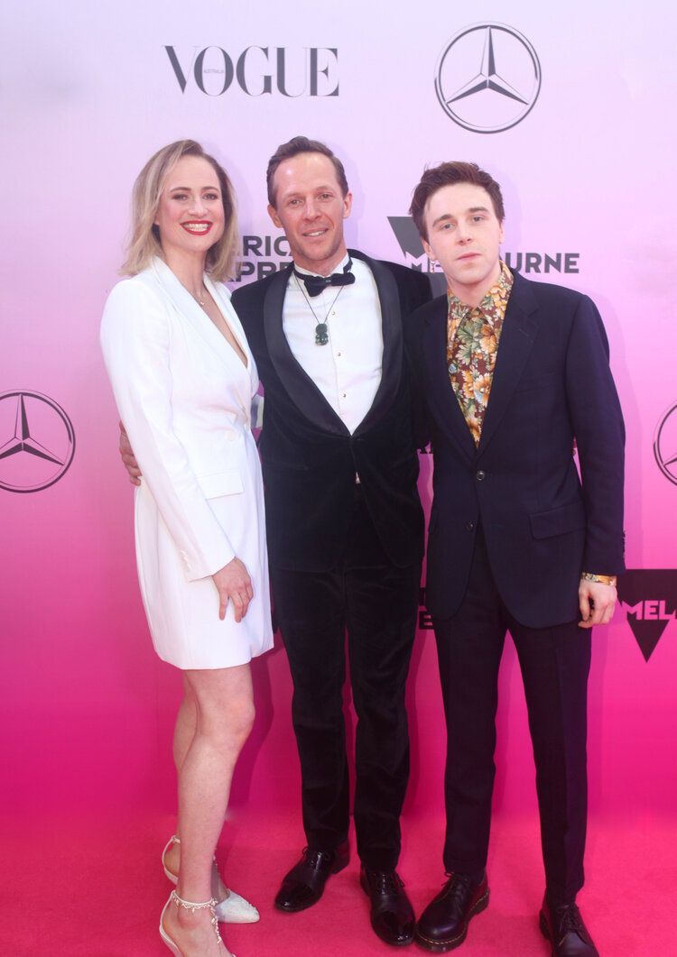 Three people are posing for a picture on a pink carpet that says vogue