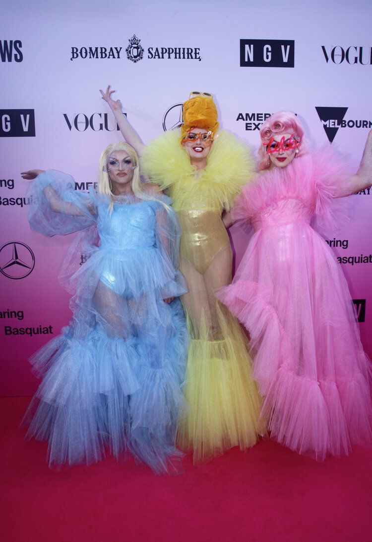 Three drag queens are posing for a picture on a red carpet.