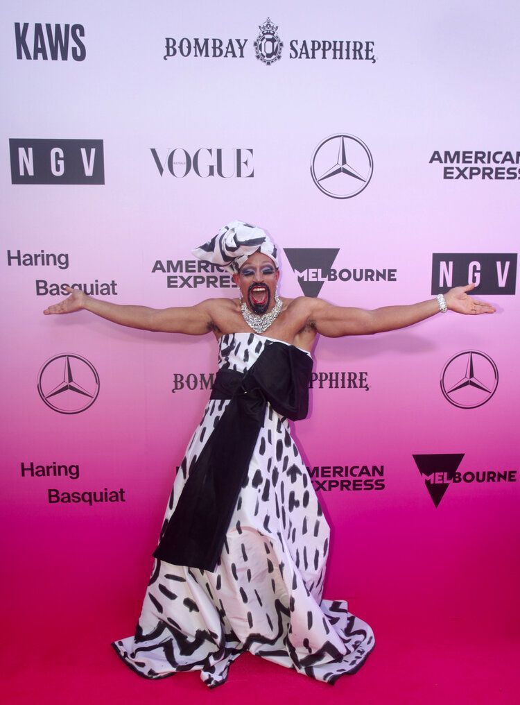 A man in a black and white dress is standing on a pink carpet.