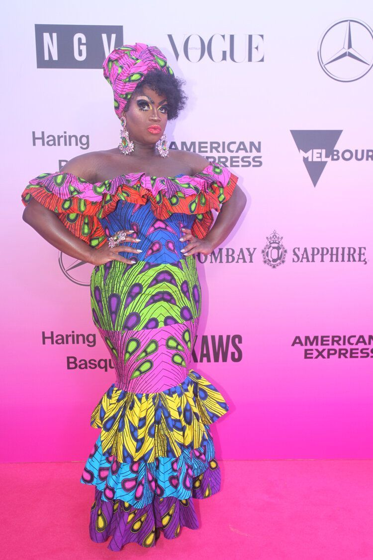 A woman in a colorful dress is standing on a pink carpet.