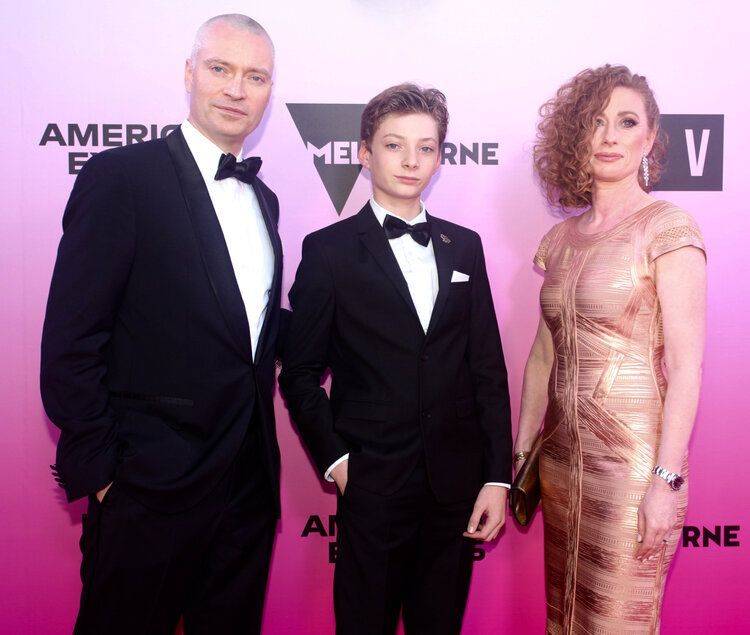 A man in a tuxedo stands next to a boy and a woman in a gold dress