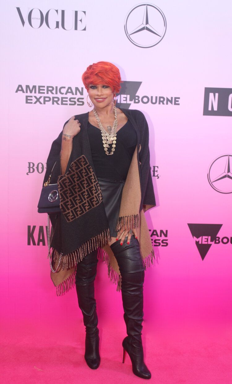 A woman with red hair is standing on a pink carpet.