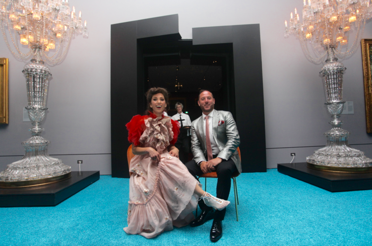 A man and a woman are sitting on a chair in front of a chandelier.