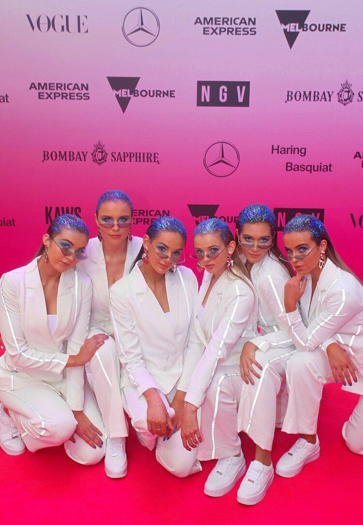 A group of women are posing for a picture on a pink background.
