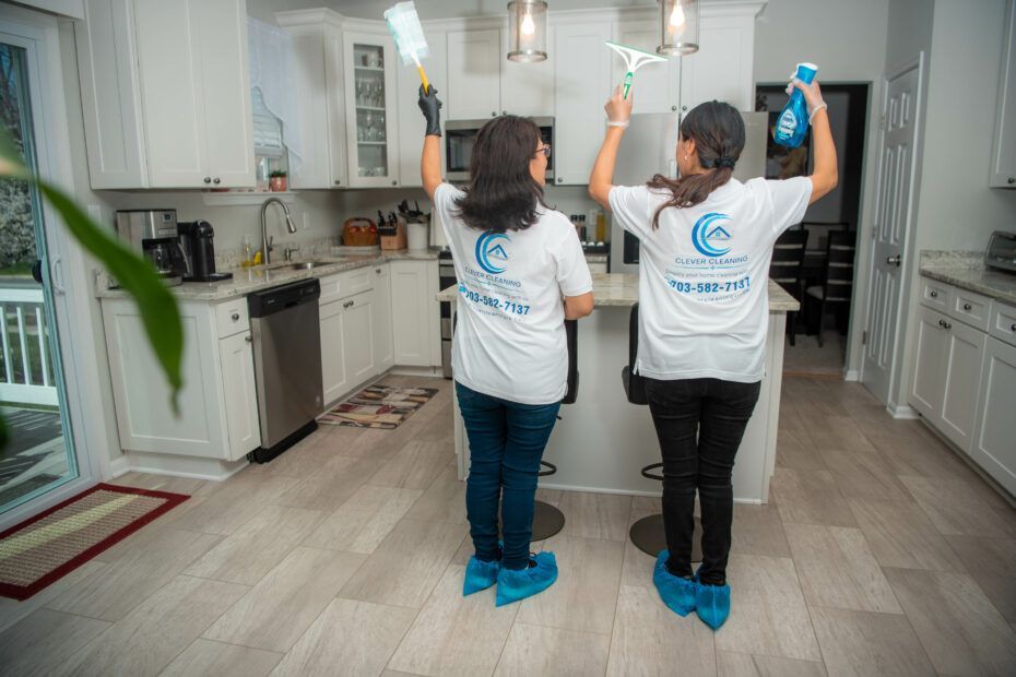 two women wearing clover cleaning shirts are cleaning a kitchen