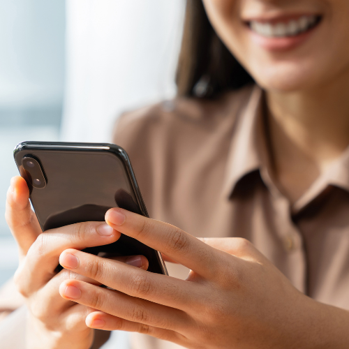 A woman is holding a cell phone in her hands and smiling.