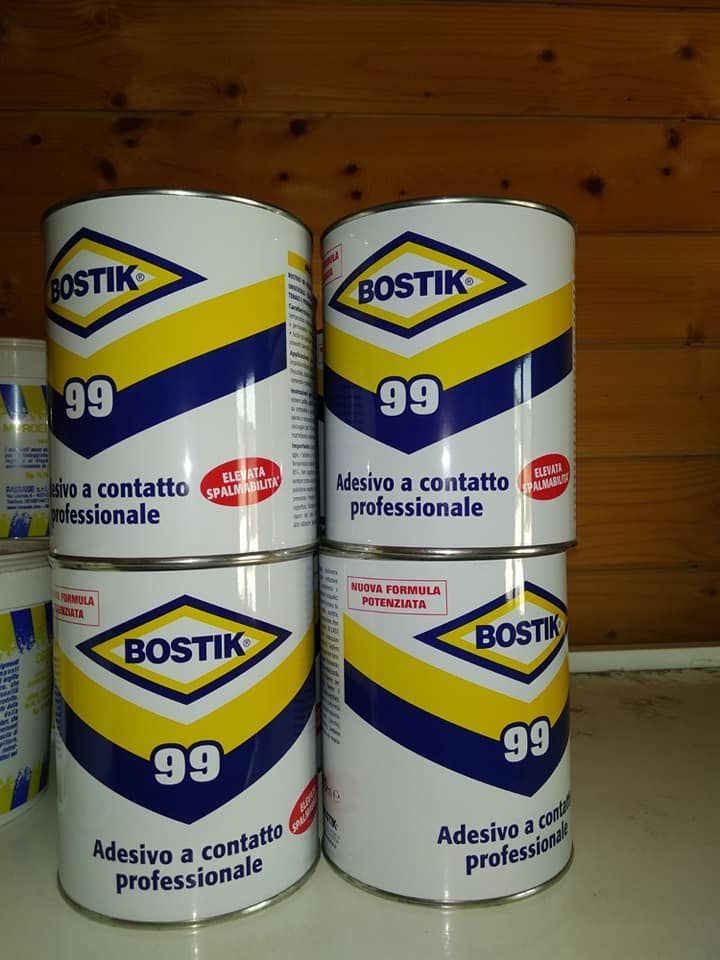 Quattro bombolette di adesivo Bostik 99 impilate. Bombolette bianche con loghi e scritte blu, gialle e rosse.