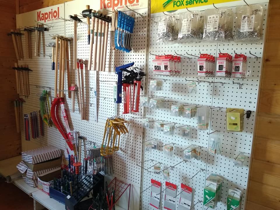 Attrezzi e ferramenta esposti su pannelli forati in un negozio di ferramenta; tra cui martelli, pinze e elementi di fissaggio.