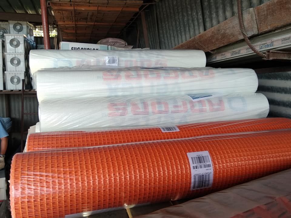 Rotoli di rete da costruzione arancione e bianca, accatastati in un'area di stoccaggio.