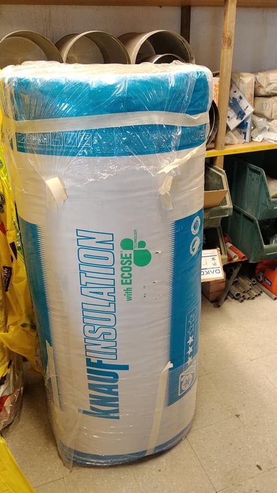 Grande rotolo cilindrico di isolante Knauf, avvolto in plastica. Etichette bianche, blu e verdi.