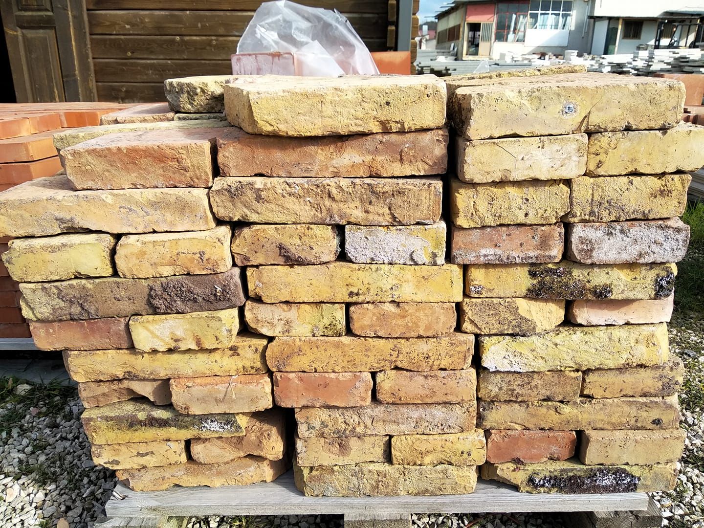 Mattoni rossi e marroni impilati su un pallet di legno all'aperto, pronti per la costruzione.