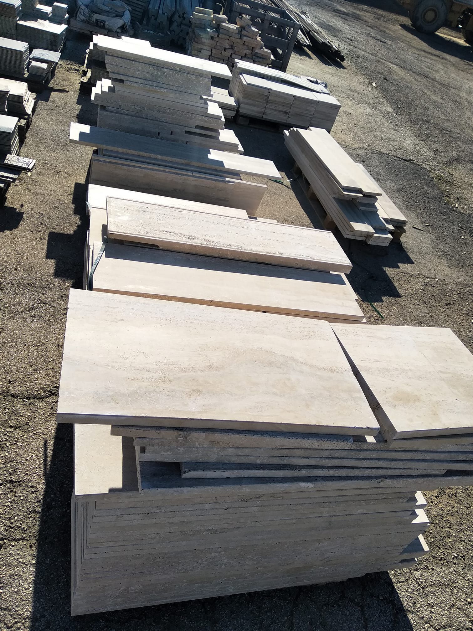 Pile di piastrelle rettangolari in pietra chiara su ghiaia, probabilmente per scopi edilizi, all'aperto.