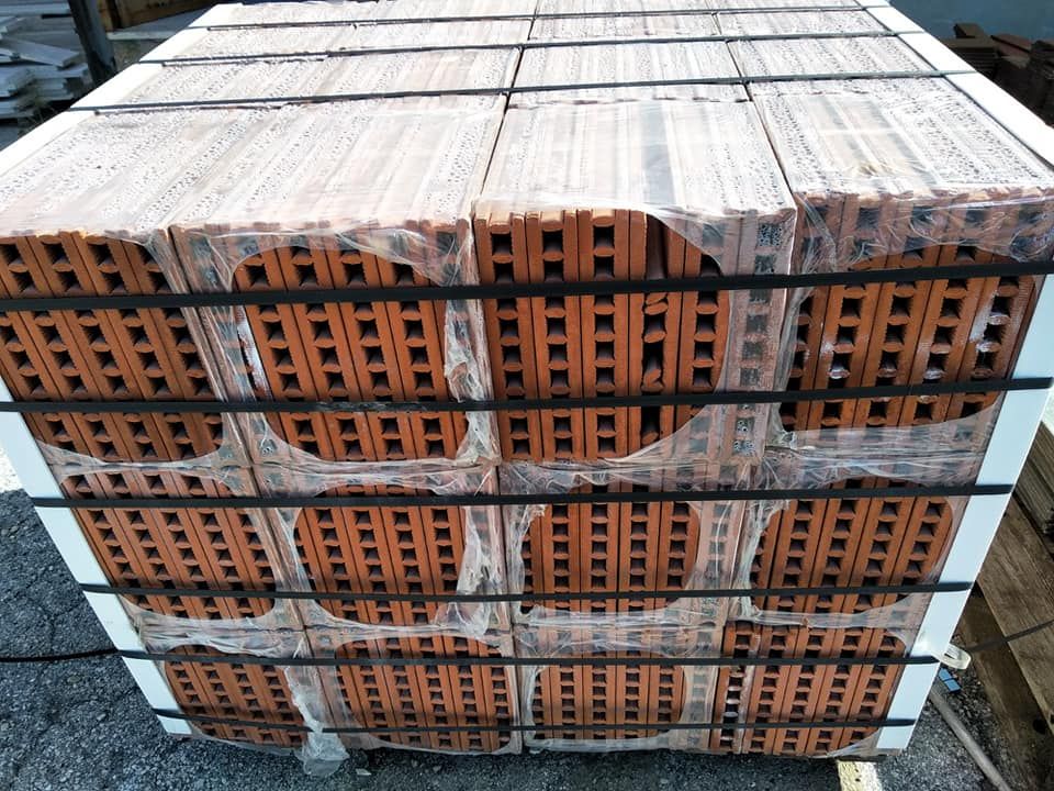 Un pallet di mattoni rosso-marroni, avvolti nella plastica e fissati con cinghie nere.