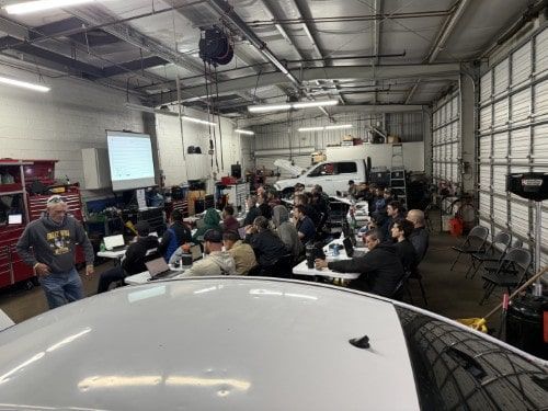 A wide-angle view of the Diag Nation training held on March 13, 2025, showing a packed garage with technicians actively participating, laptops open, and diagnostic material projected on-screen.