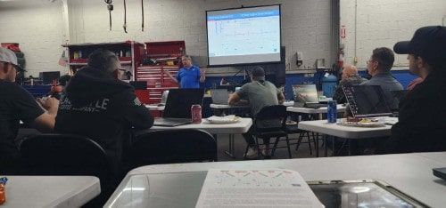 A classroom-style diesel diagnostics training session led by Adam Robertson of Diag Nation in March. Attendees are seated at tables with laptops and notebooks, while a projected presentation shows waveform analysis. Three of the shop’s technicians are seated in the back row, participating in this high-level training tailored for advanced diesel diagnostics.