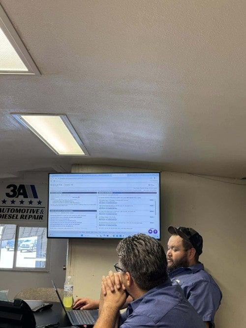 Two technicians attentively follow a presentation on a wall-mounted screen during a Lunch & Learn session led by Service Manager Edgar Norris at 3A Automotive & Diesel Repair.