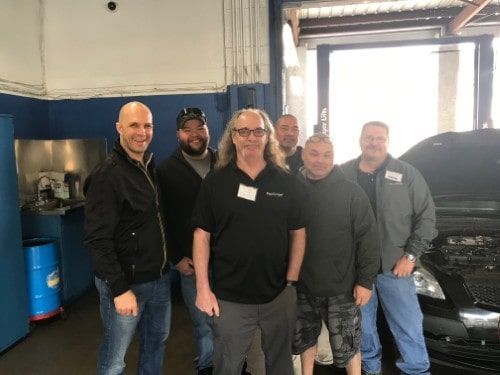 Eric Ziegler stands with a group of attendees, smiling for a group photo inside the garage during his Advanced Technical Training event.