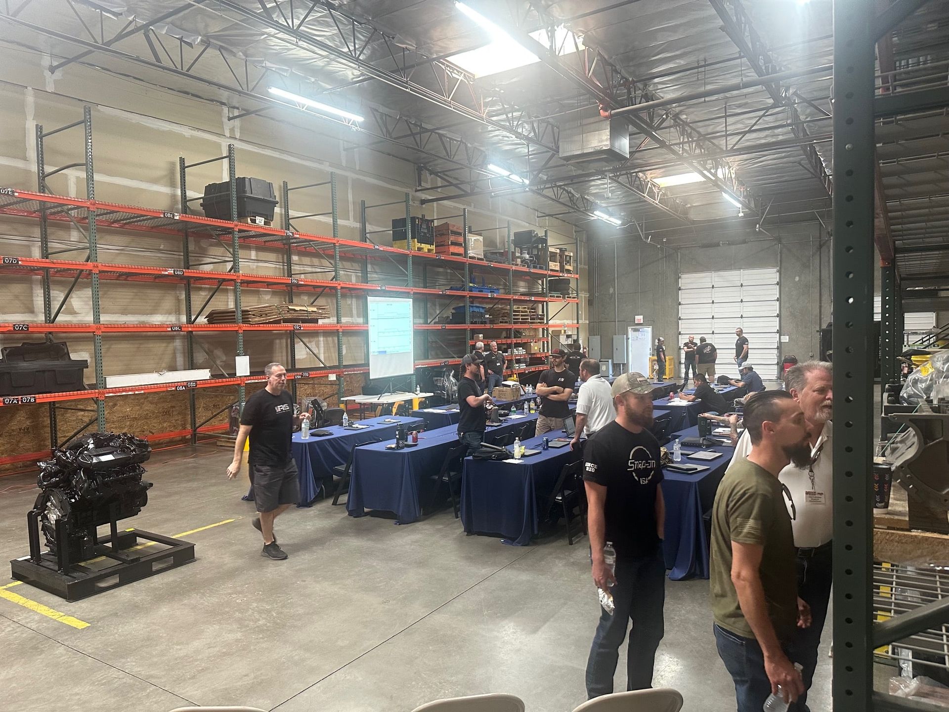 A group of team members sits around a conference table with food and drinks, engaged in a Lunch & Learn training session led by Service Manager Edgar Norris, with a digital dashboard displayed on the screen at 3A Automotive & Diesel Repair.