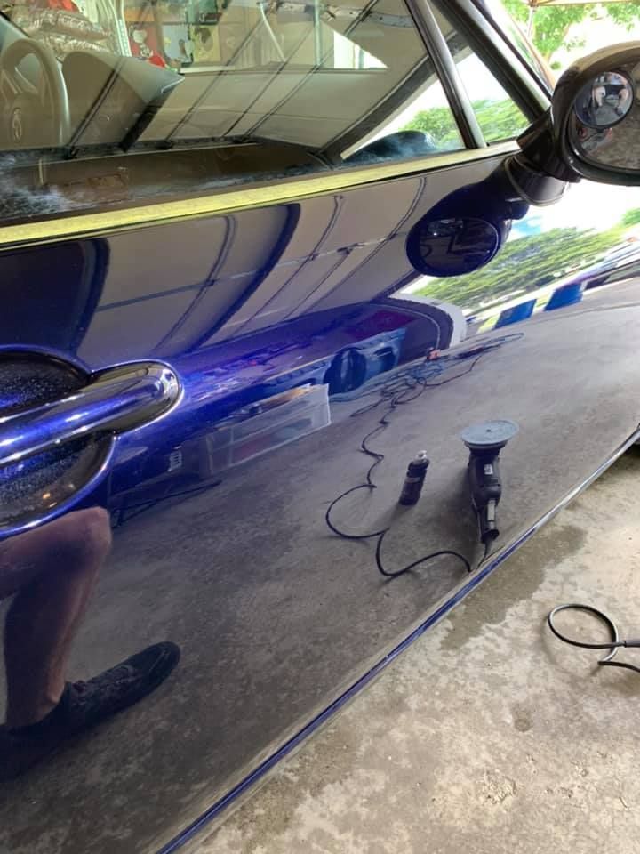 A person polishing a shiny blue car's side panel with a machine in an outdoor setting.