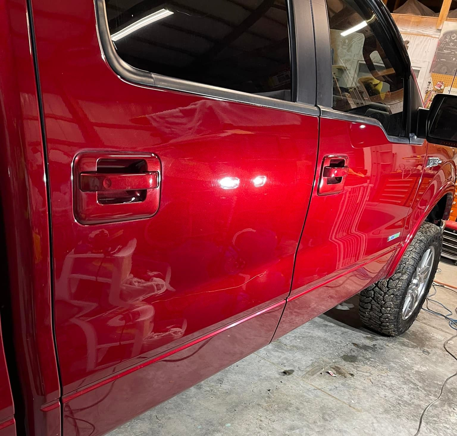 Red pickup truck door and wheel, close-up shot indoors, shiny paint.