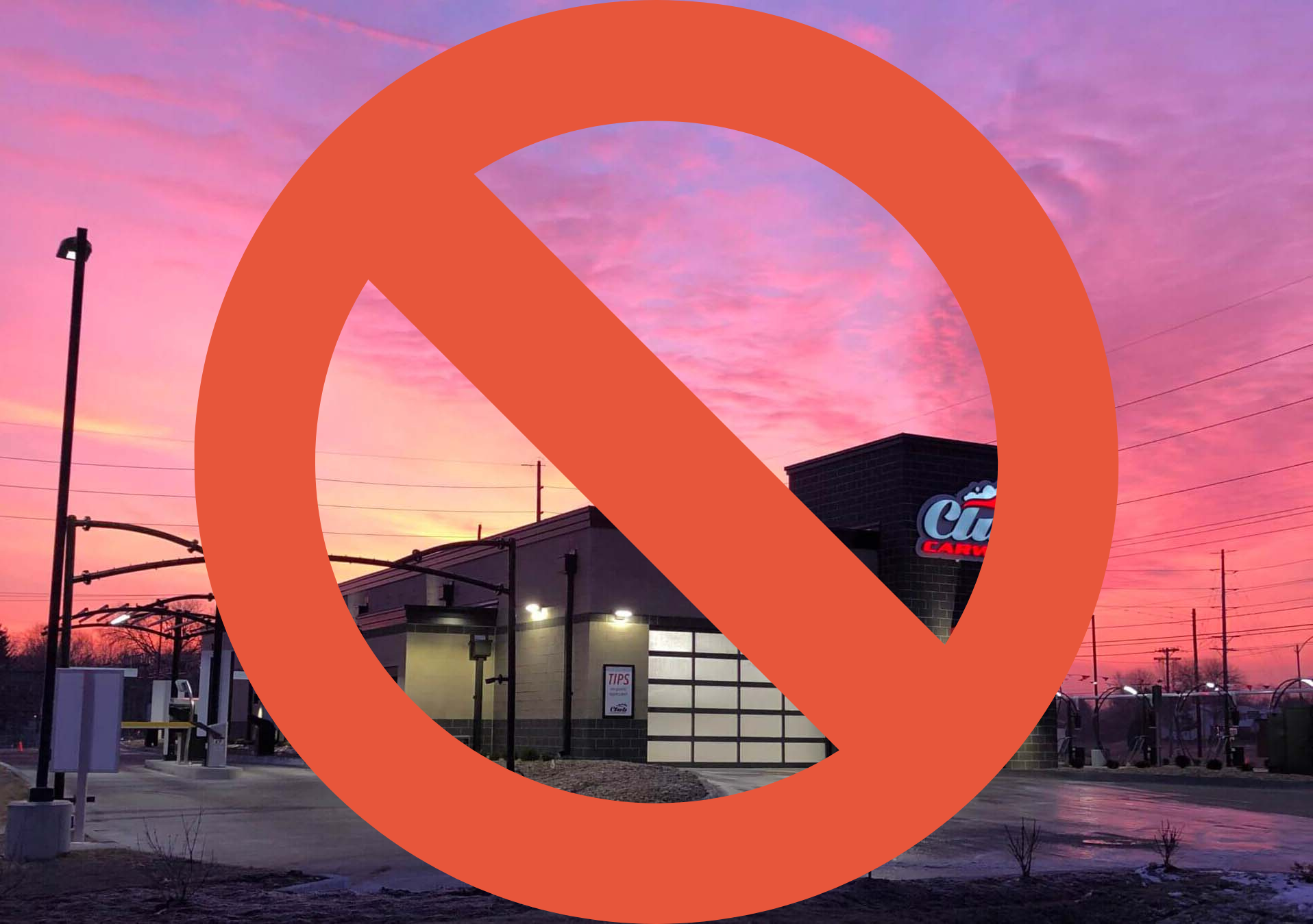 Car wash crossed out with a large orange prohibition sign, against a sunset sky.