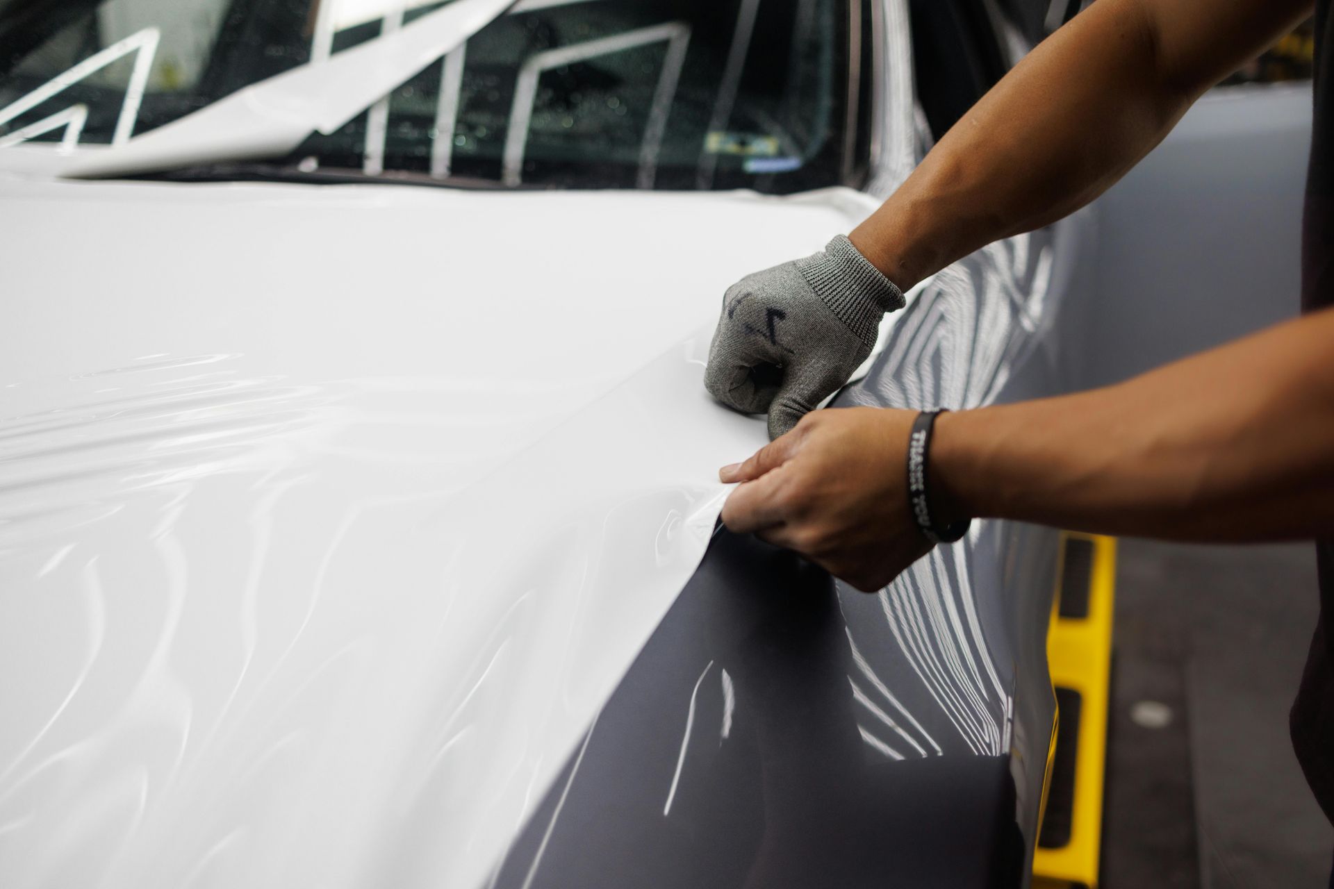 Hands of a person wrapping a car in white vinyl.