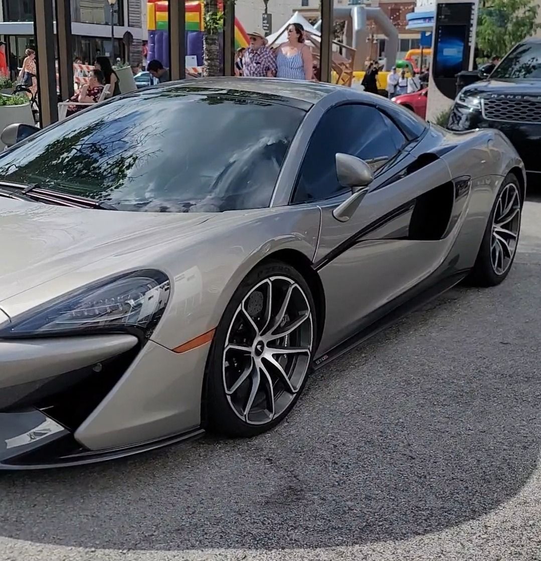 Silver McLaren sports car parked on a city street, daytime.