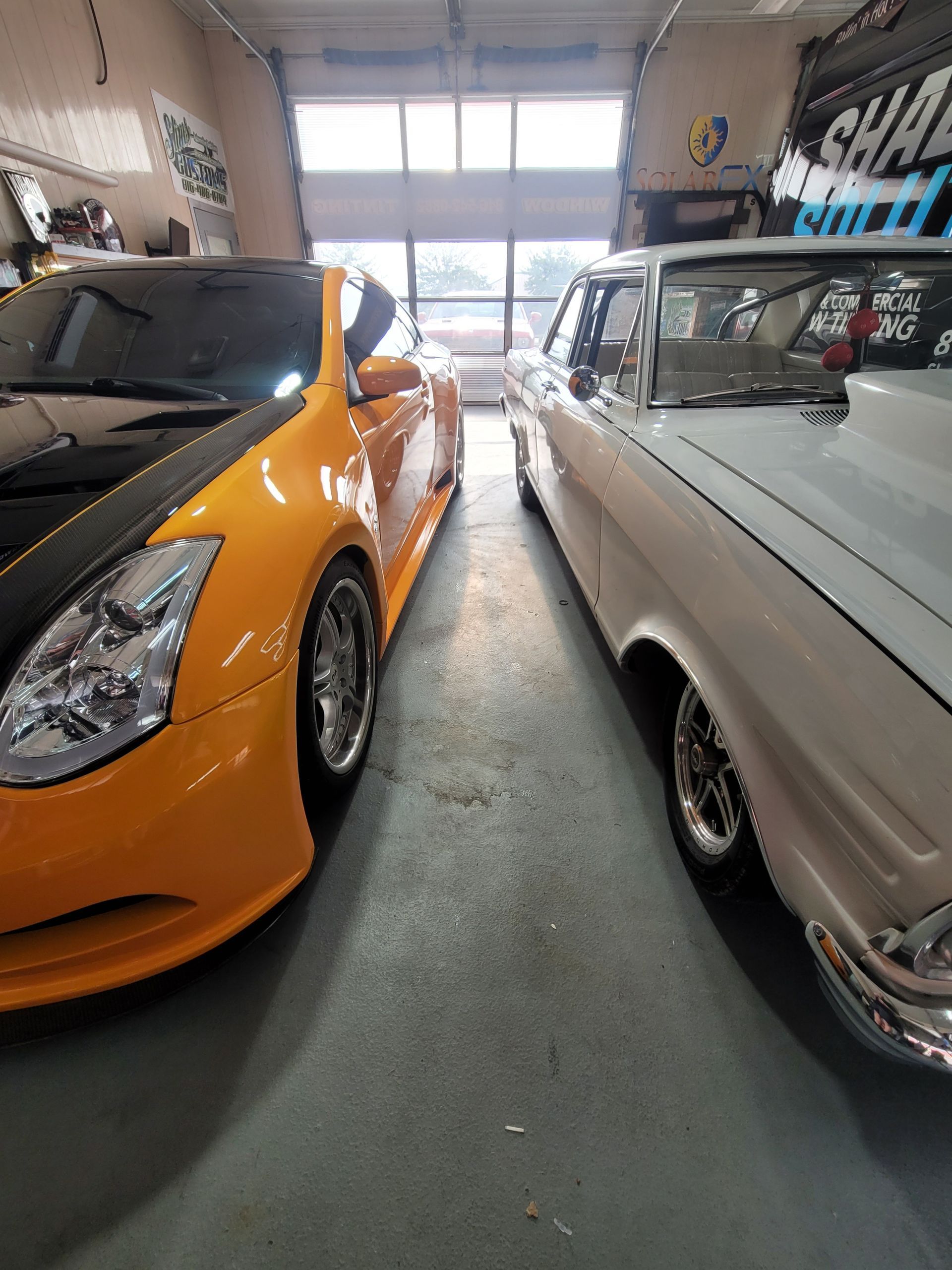 Orange sports car and white classic car parked inside a garage.