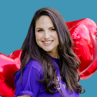 A woman in a purple shirt is holding a red heart shaped balloon.