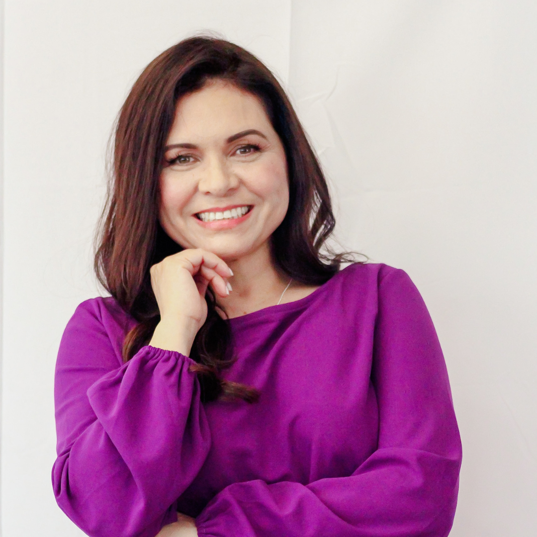 A woman in a purple shirt is smiling with her hand on her chin