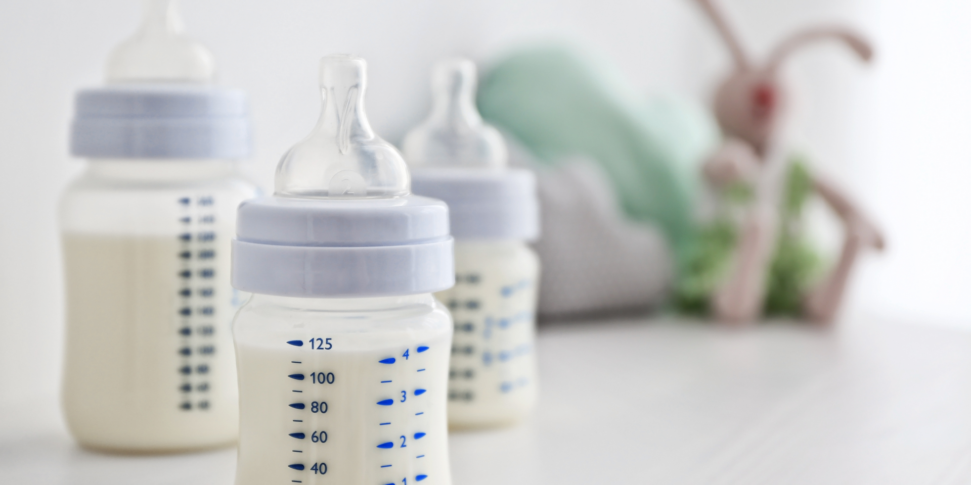 Three baby bottles filled with milk are lined up on a table.