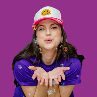 A woman wearing a hat with a smiley face on it blowing soap bubbles