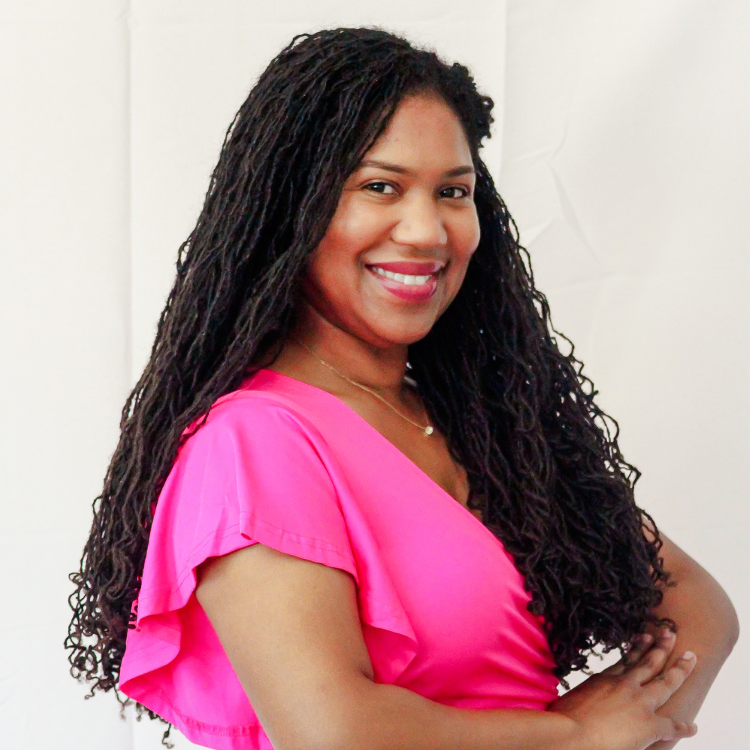 A woman with long curly hair is wearing a pink top and smiling