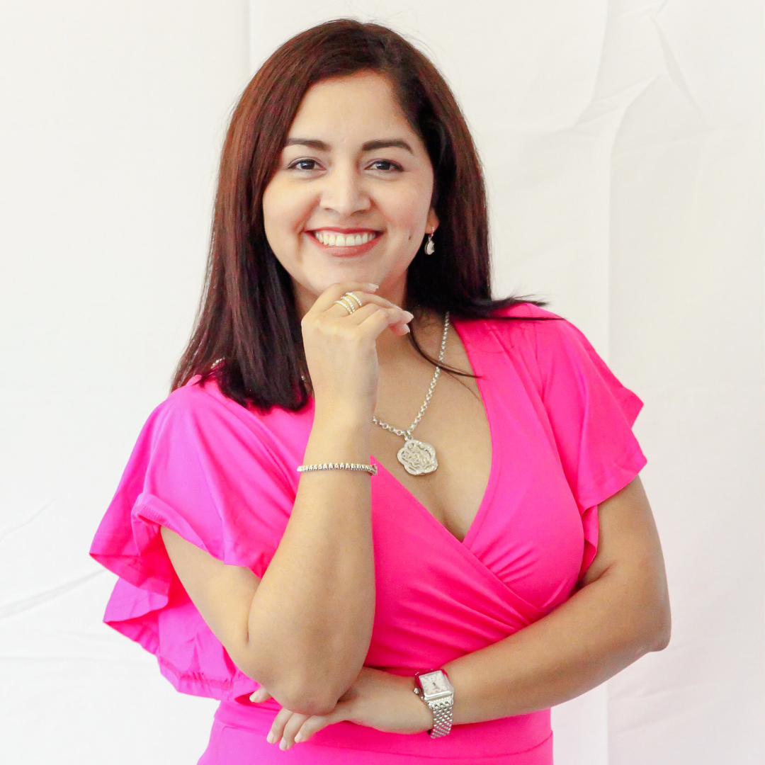 A woman in a pink dress is smiling with her hand on her chin.