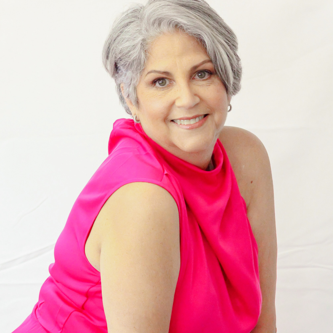 A woman with gray hair is wearing a pink dress and smiling.