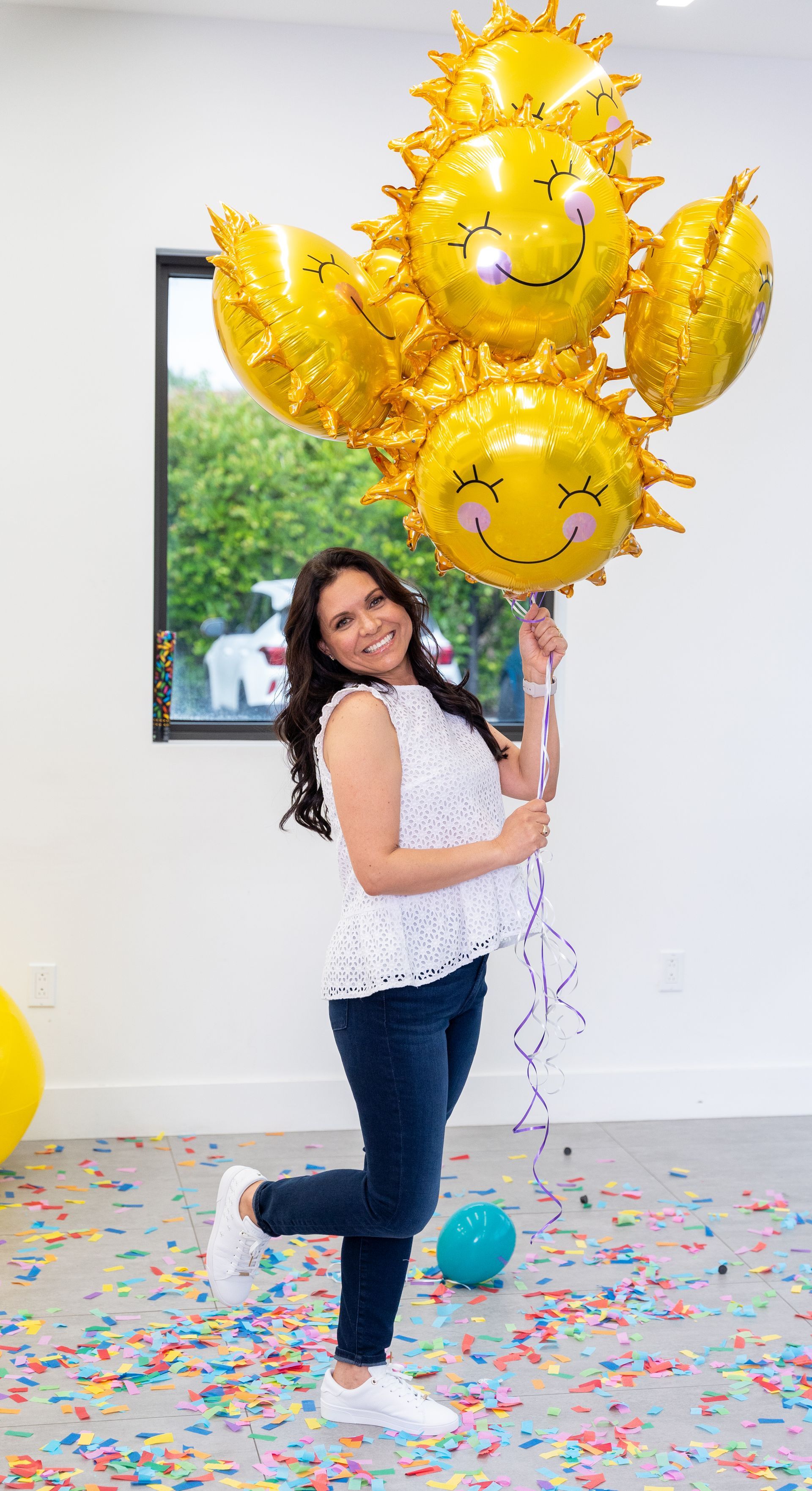 A woman is holding a bunch of yellow balloons with smiley faces on them.