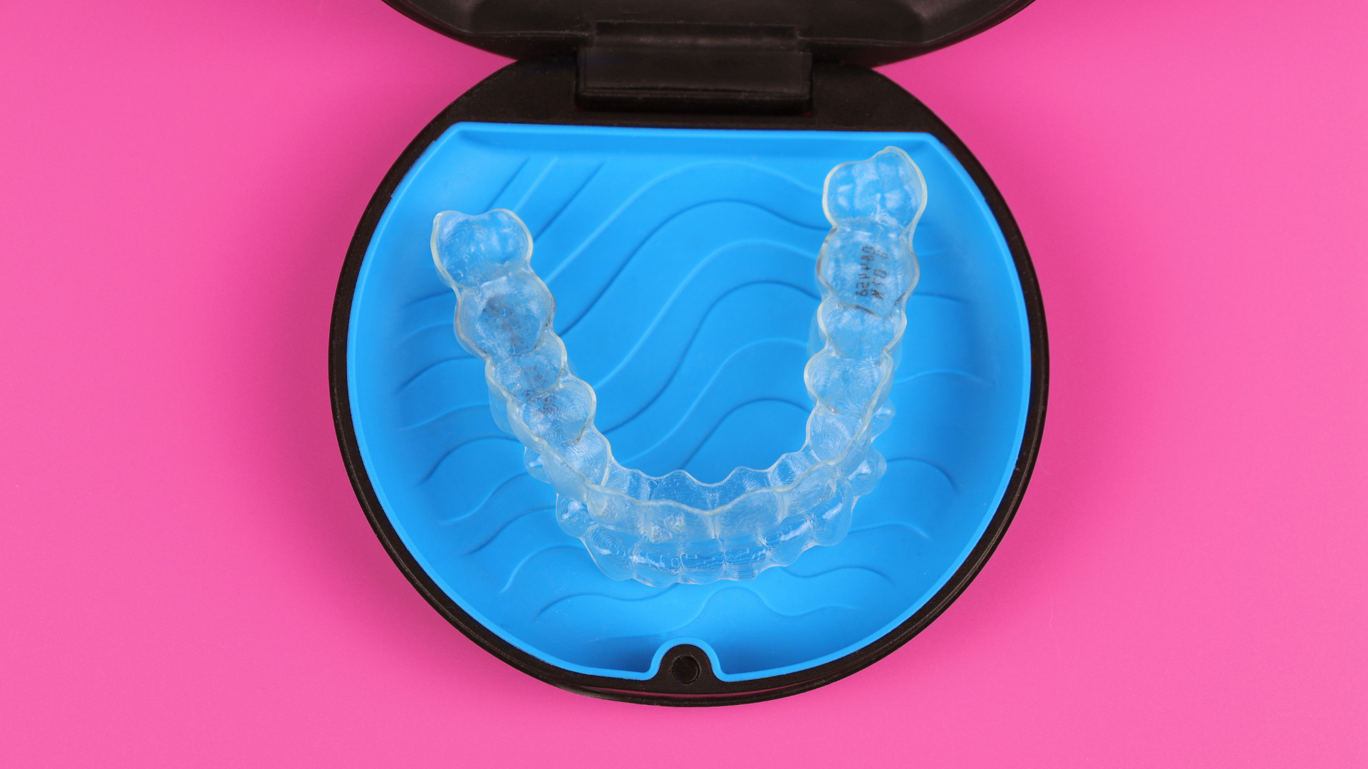 A clear retainer in a blue case on a pink background.