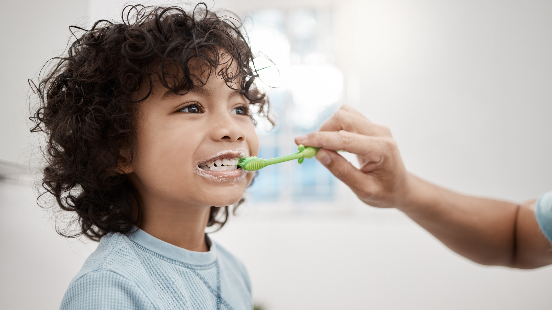 A young boy is brushing his teeth with a green toothbrush.