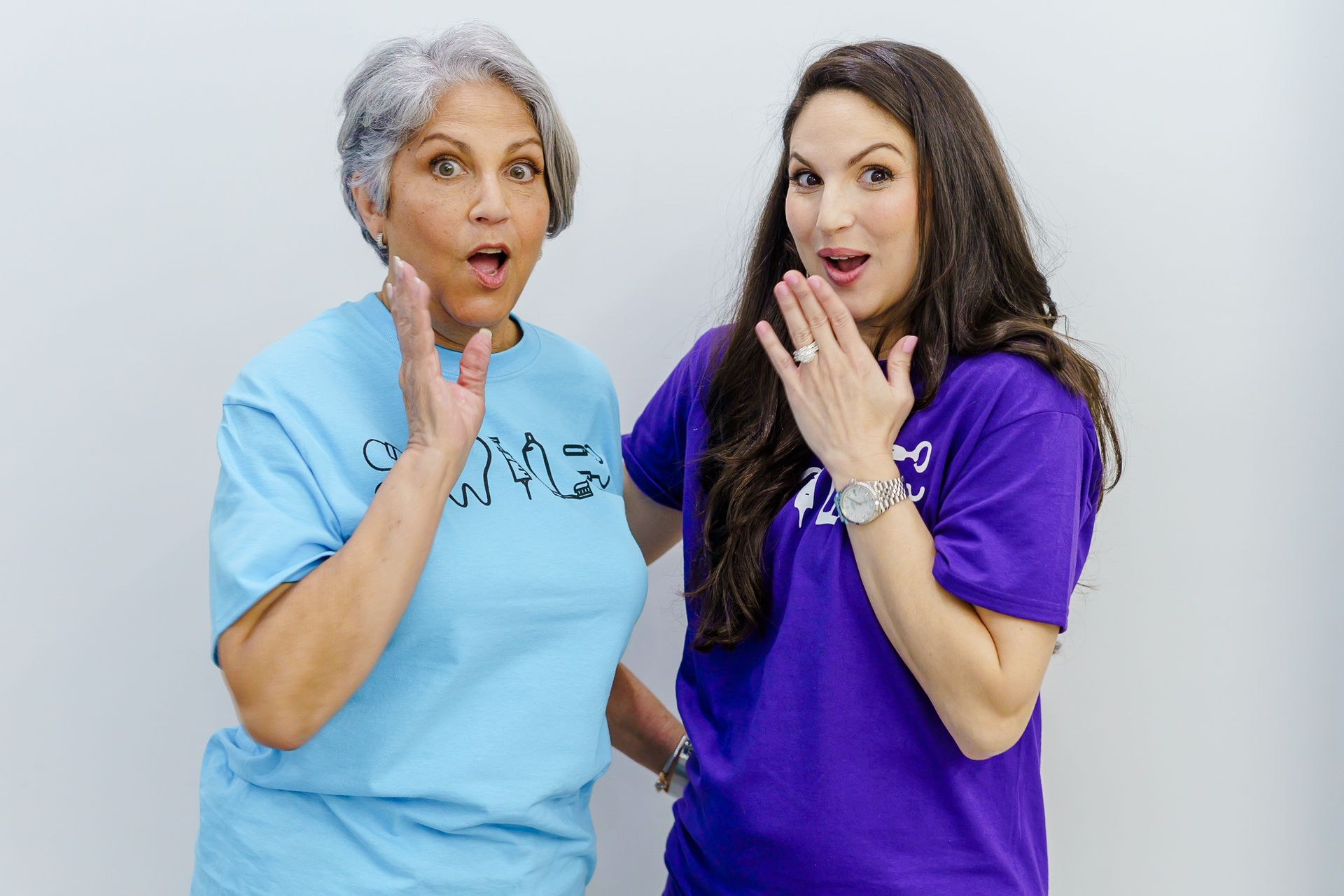 Two women are standing next to each other and one is wearing a blue shirt and the other is wearing a purple shirt.