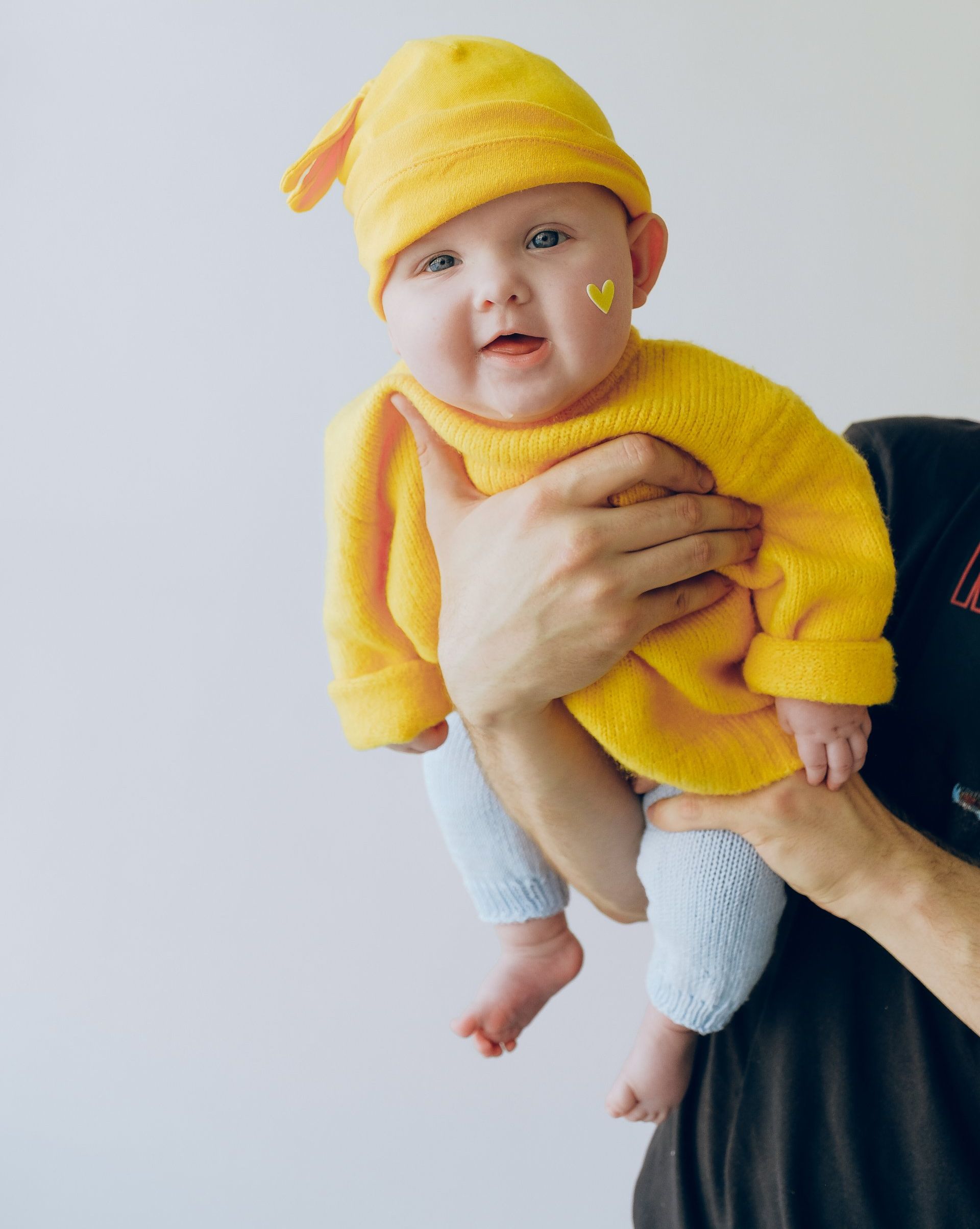 A person is holding a baby wearing a yellow hat