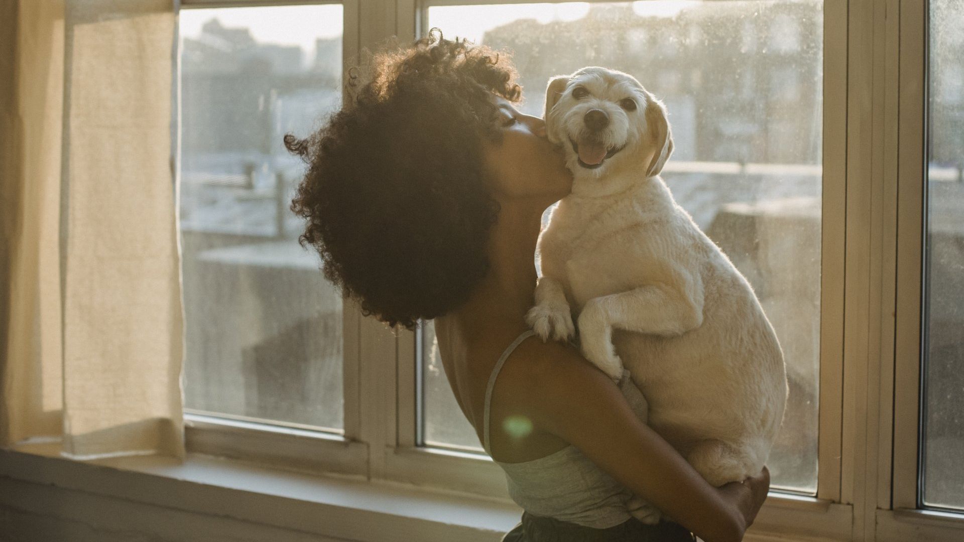 Woman hugging and kissing her dog in front of the window
